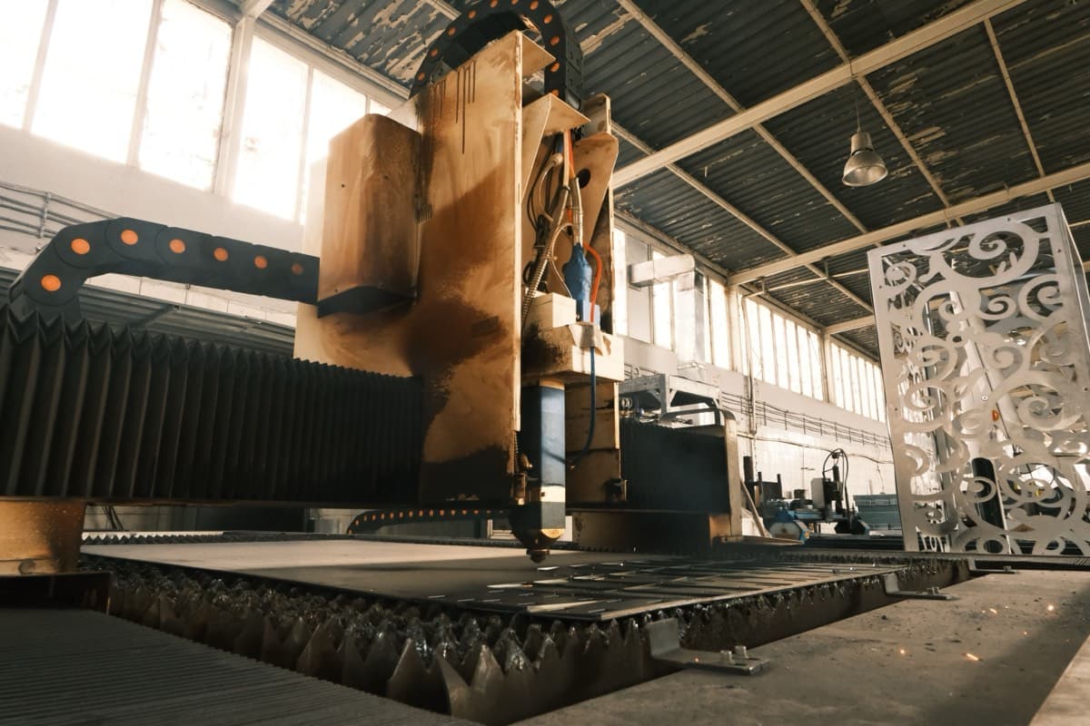 A CNC table cutting a sheet of steel, with a finished panel standing beside it.