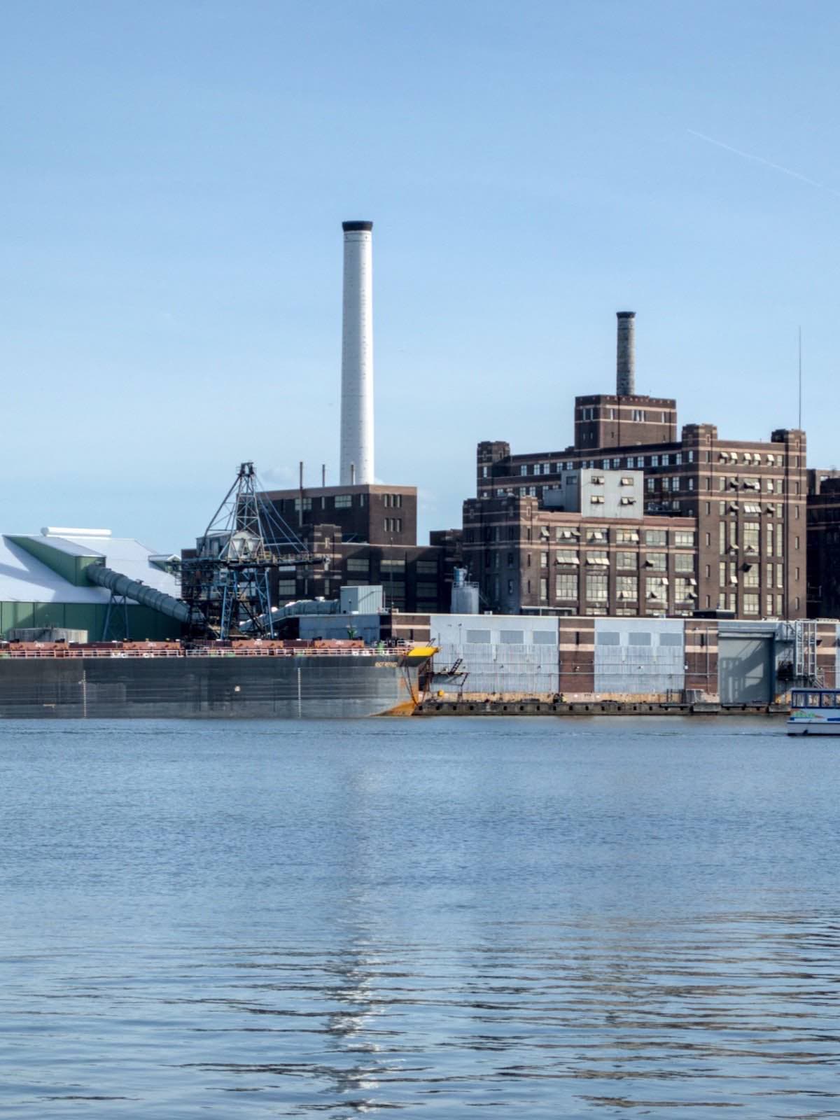 A working waterfront at midday: cranes, brick warehouses and a barge along the quay.